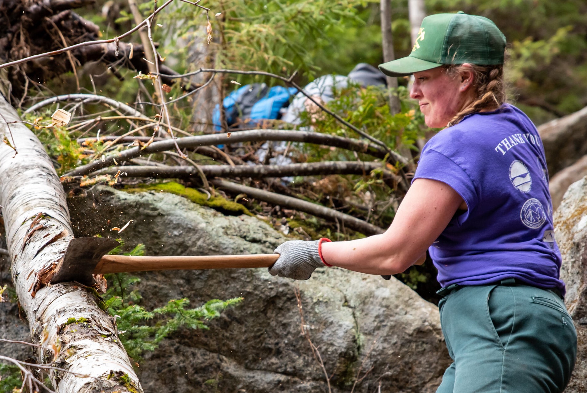 woman wearing a hat uses an axe to cut a tree